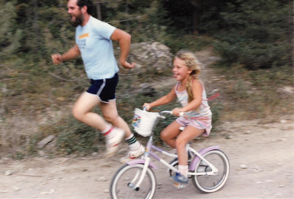 A photograph of Beth as a child riding her bike alongside her father running