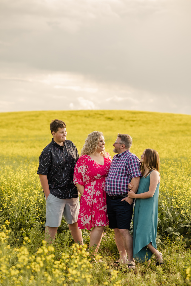 A recent photograph of Beth standing in a canola field with her children and partner